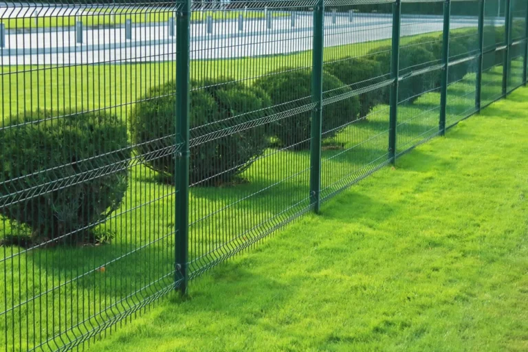 Zöld színű 3D táblás kerítés gondozott parkos környezetben, gyep és sövény mellett